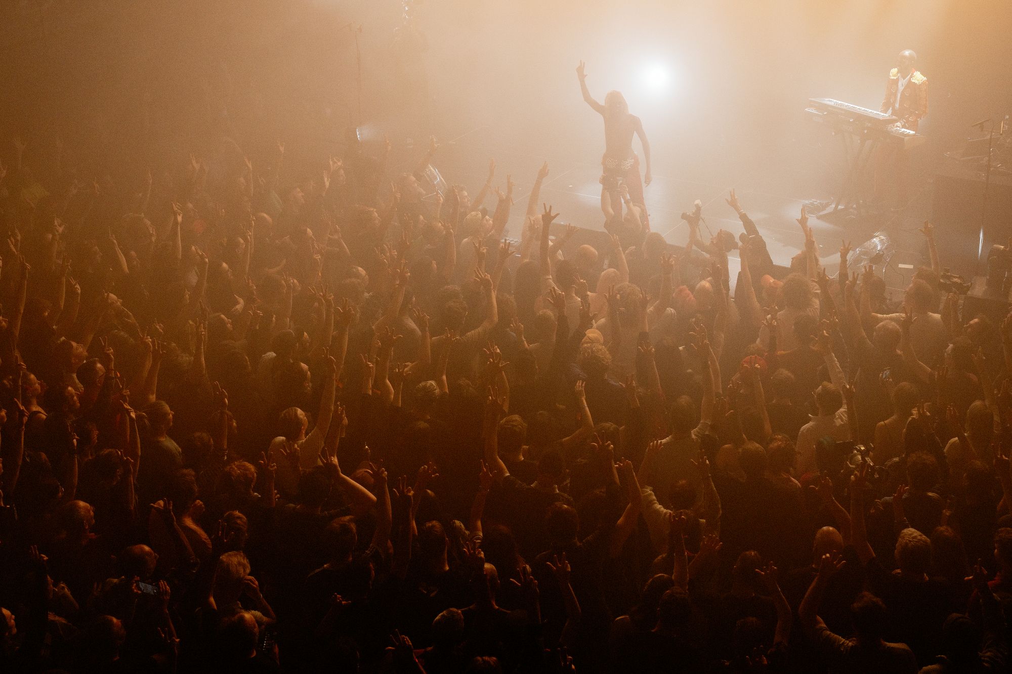 The artist Kabeaushé on stage at Le Guess Who?, pictured in the top corner of the photograph. The rest of the photograph is filled with an ecstatic audience with arms raised in the air. 